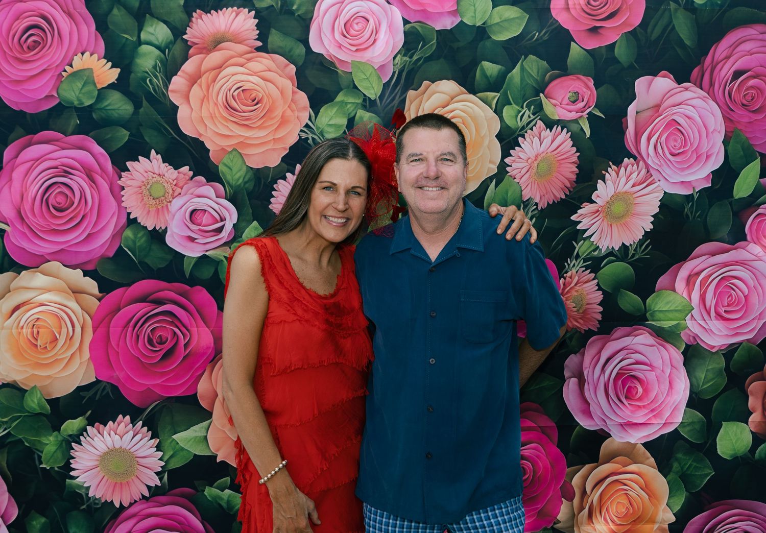 Smiling couple in festive attire posing together in front of a colorful painted floral rose wall backdrop.
