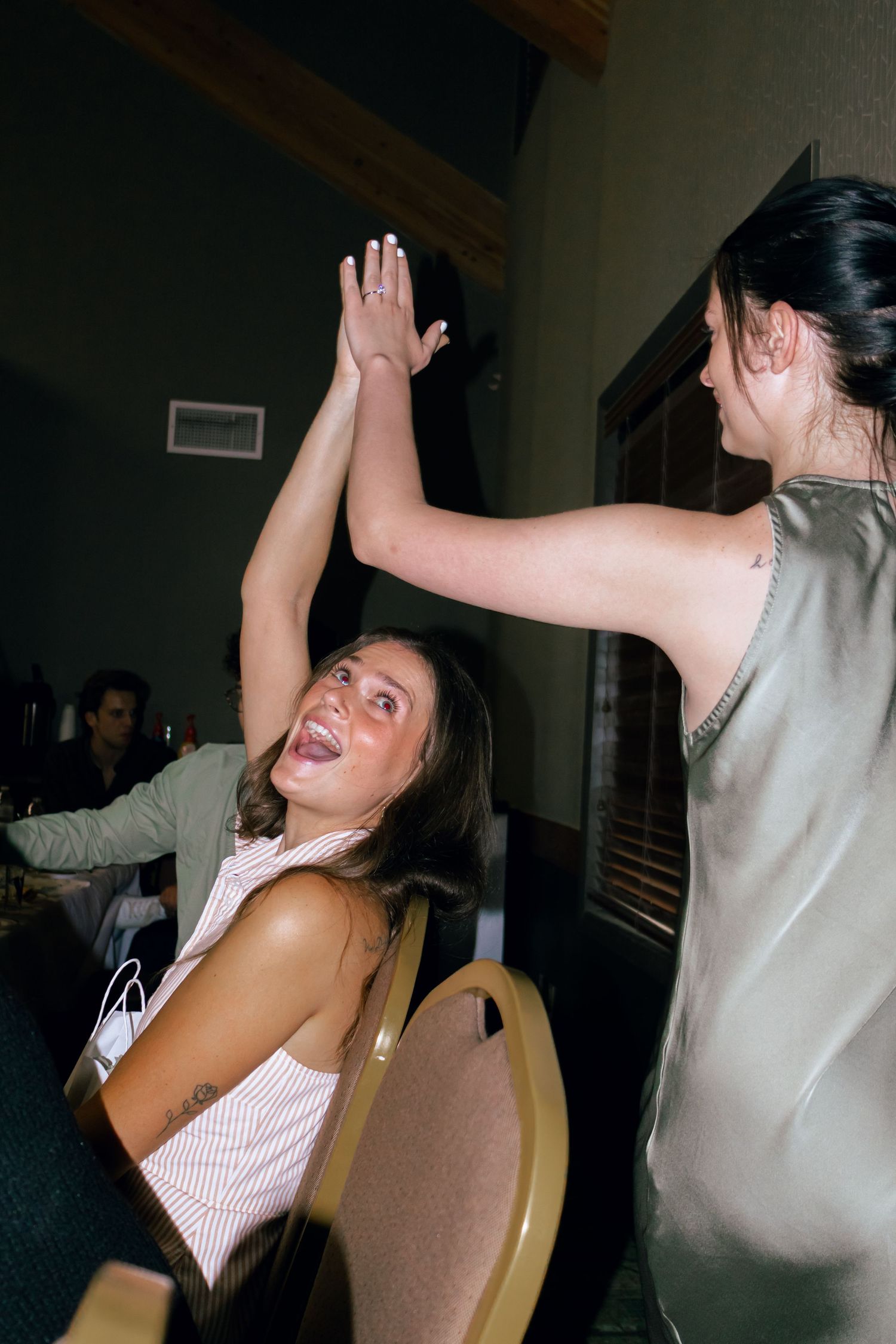 Two women giving a high five and laughing at a wedding reception.