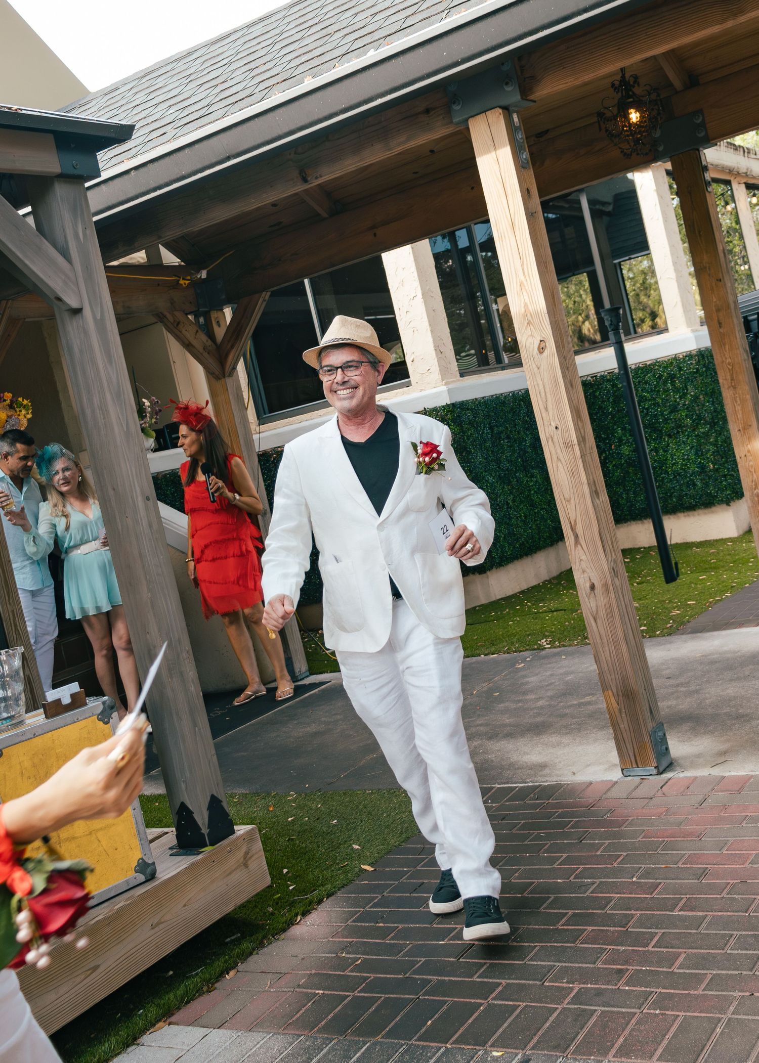 Man in white suit and straw hat walks confidently through outdoor venue at a Kentucky Derby-themed party.
