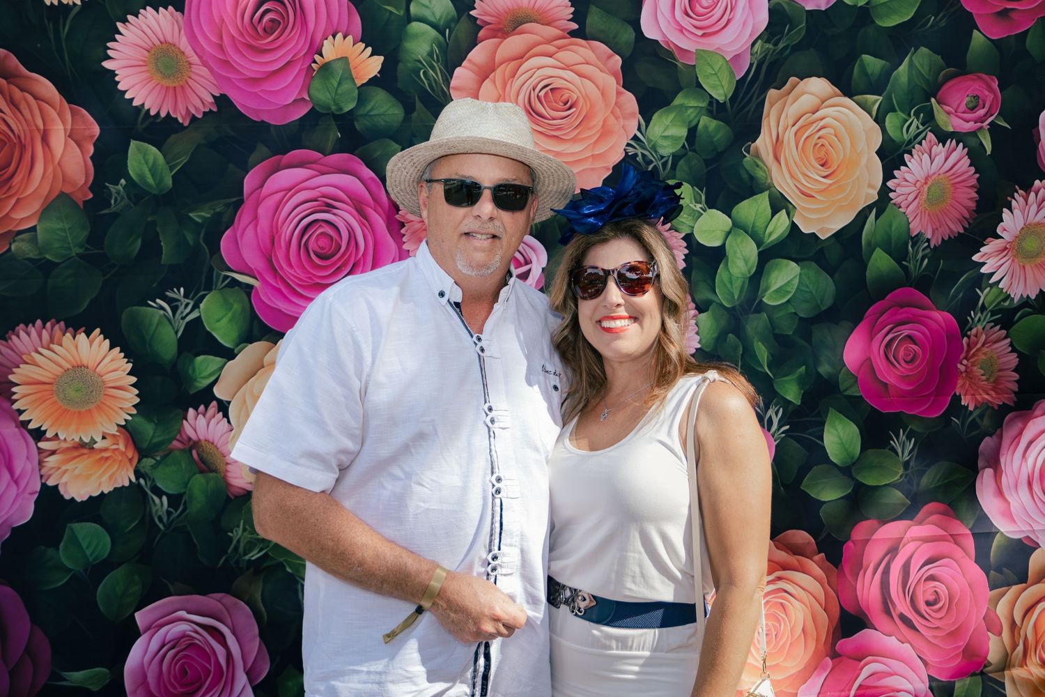 Smiling couple posing in front of a colorful painted rose floral backdrop at an outdoor Derby event.