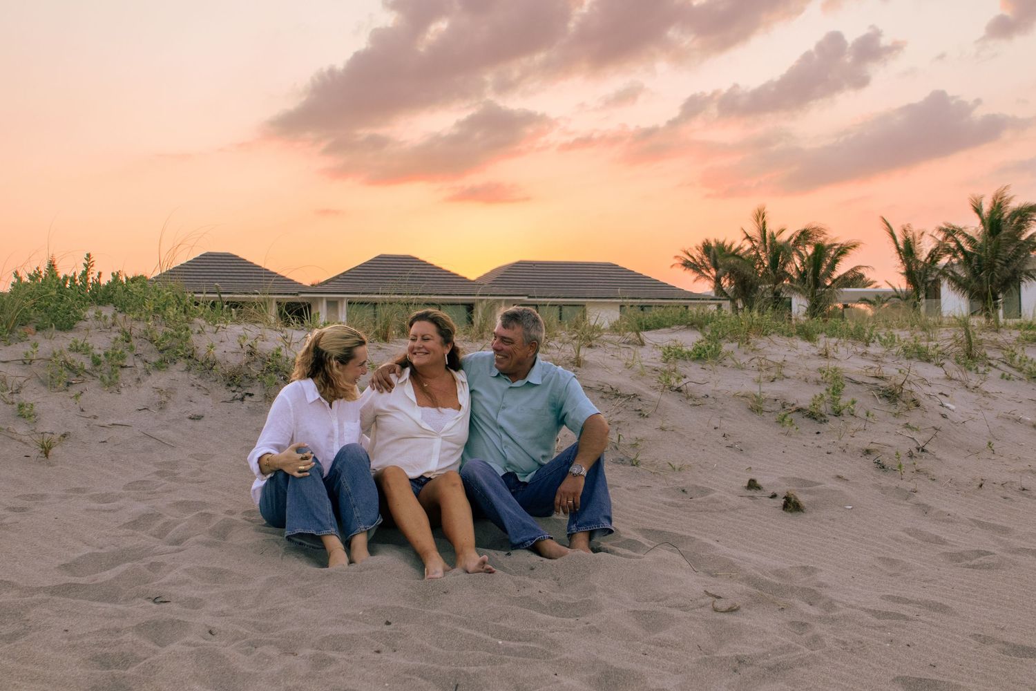 Happy family of three sitting together on sandy beach during a colorful sunset.