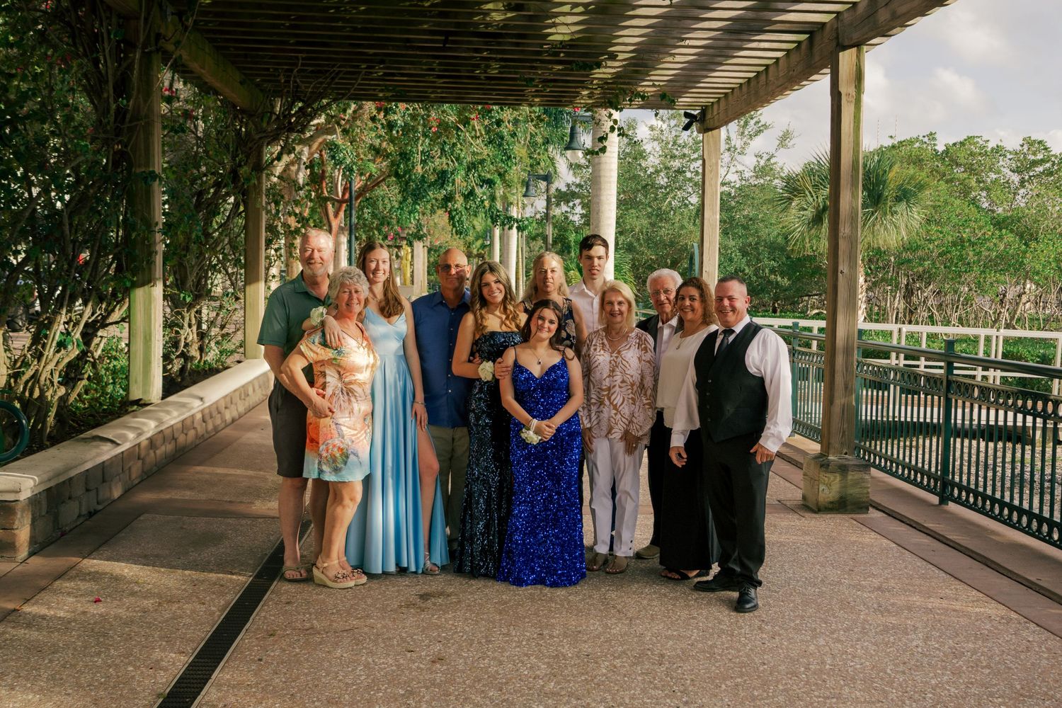 A group of elegantly dressed family members pose together under a pergola at a waterfront prom venue in Florida.