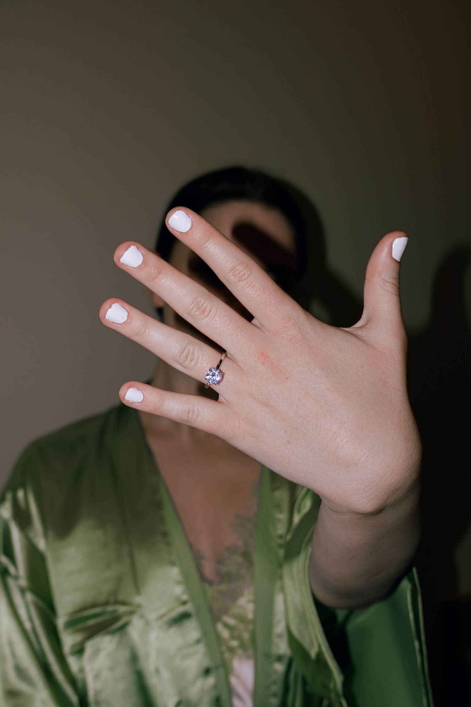 Bride in green satin robe showing diamond engagement ring on her hand.