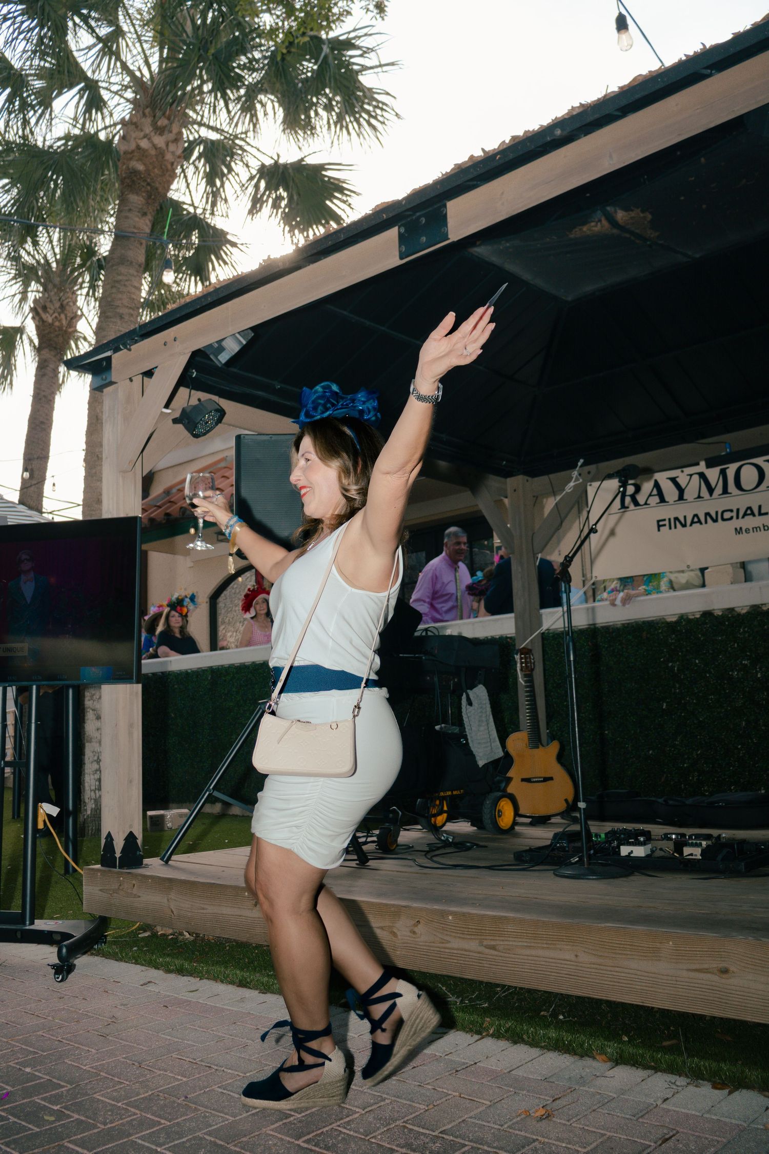 Woman in white dress dancing with raised arm at outdoor Raymond James sponsored event.