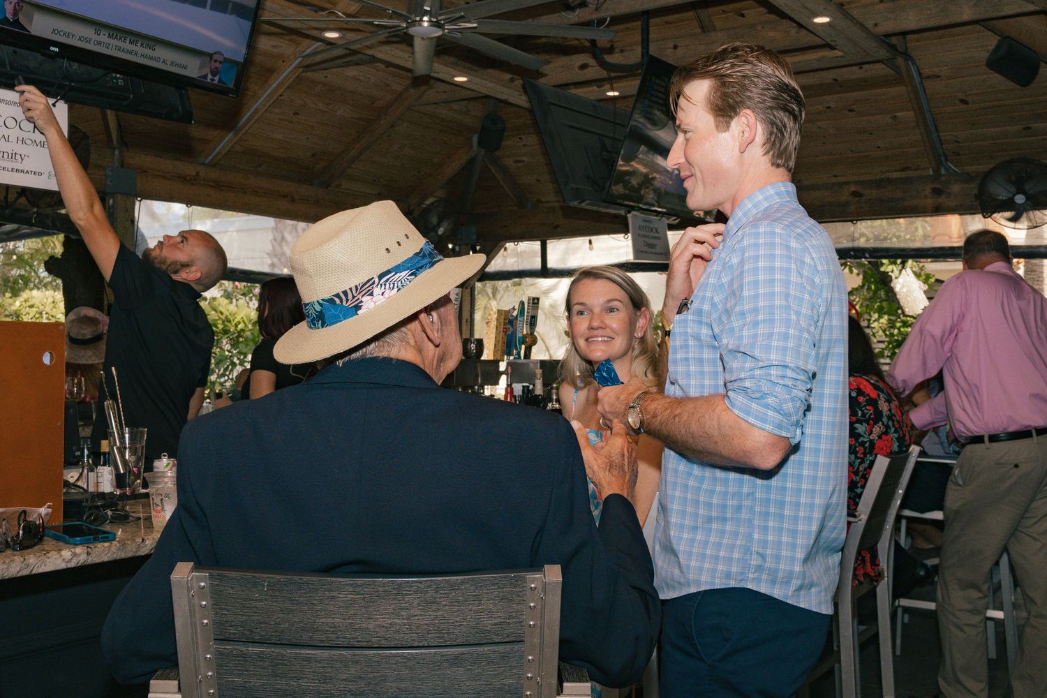 Three people in casual attire conversing at an outdoor bar under a covered patio.