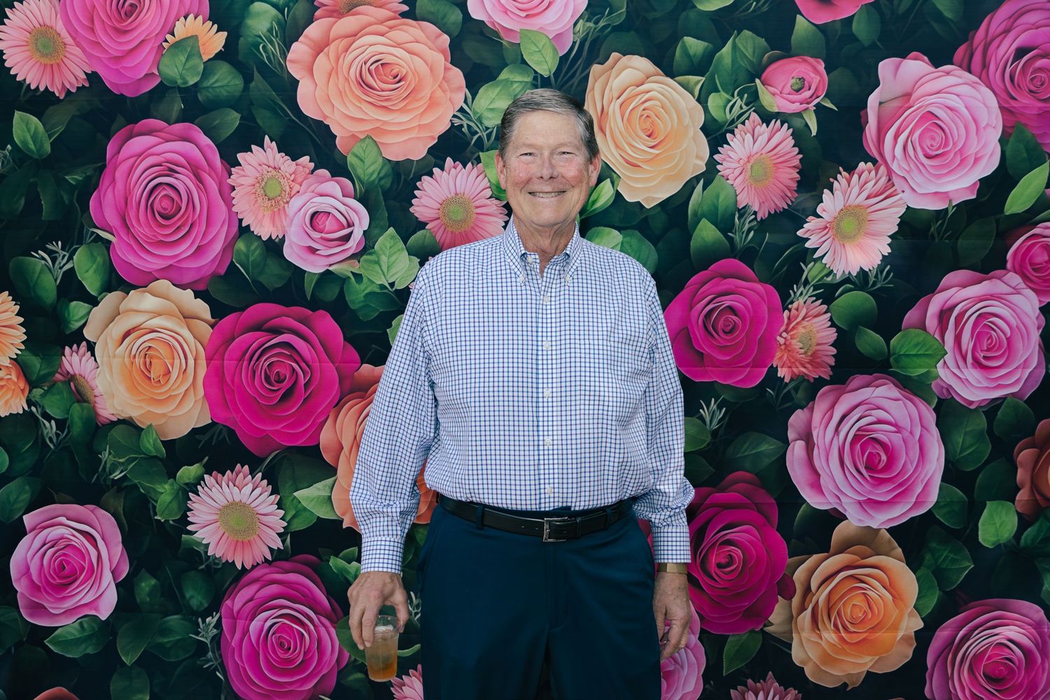 Smiling man in a blue striped shirt posing in front of a vibrant painted floral rose backdrop.