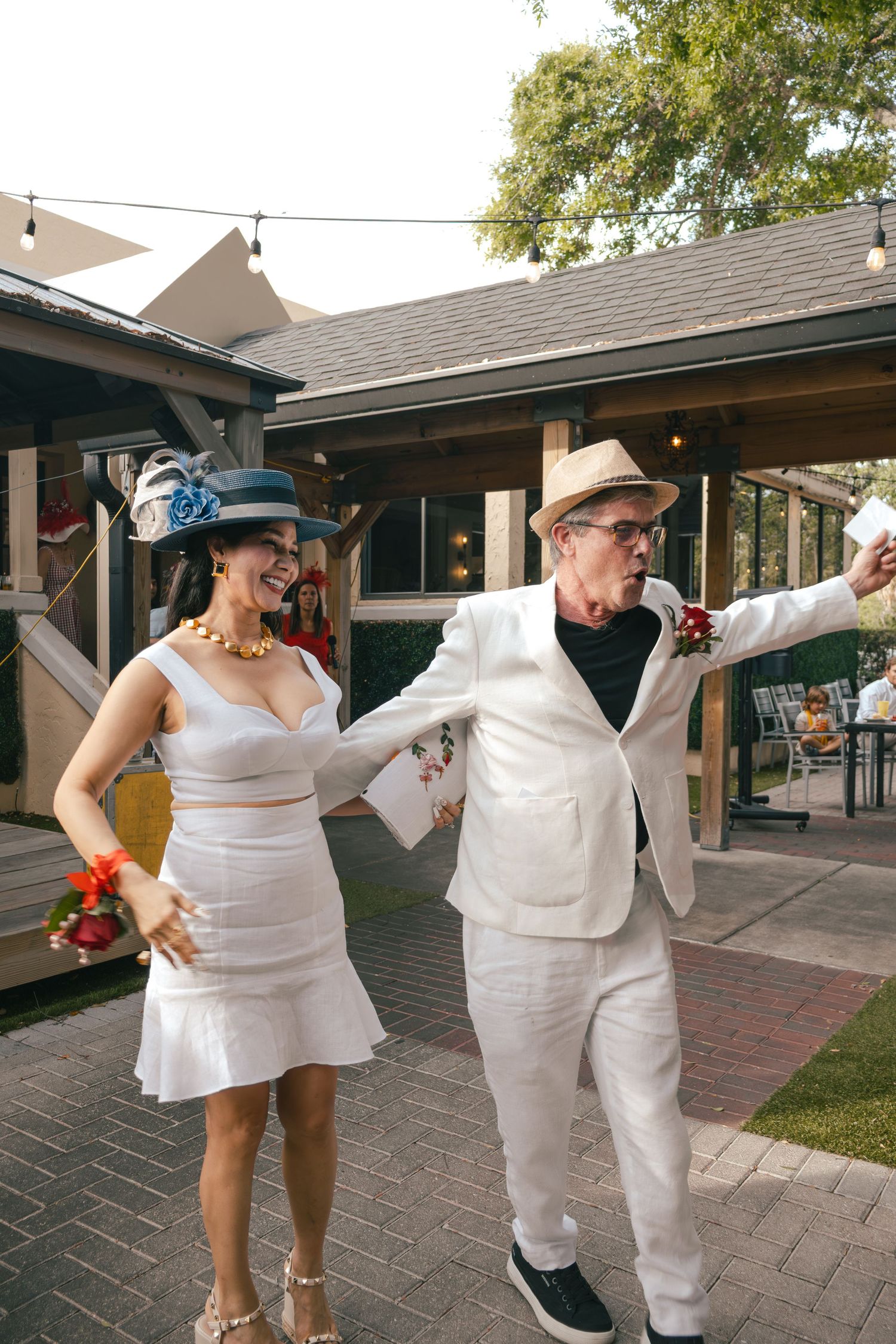 Couple in white outfits and festive hats dancing together at outdoor Derby party.