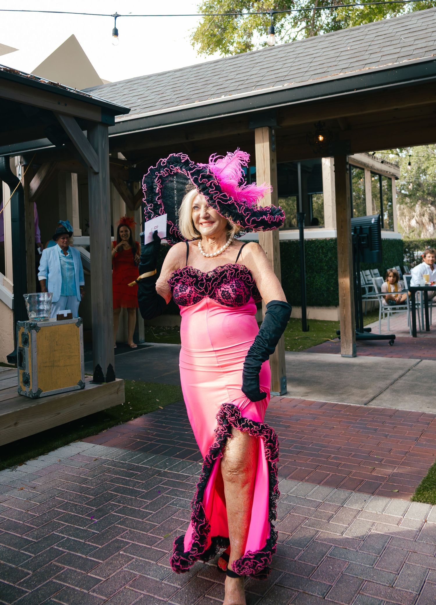 Woman in bold pink gown with feathered black hat at Kentucky Derby fashion event.