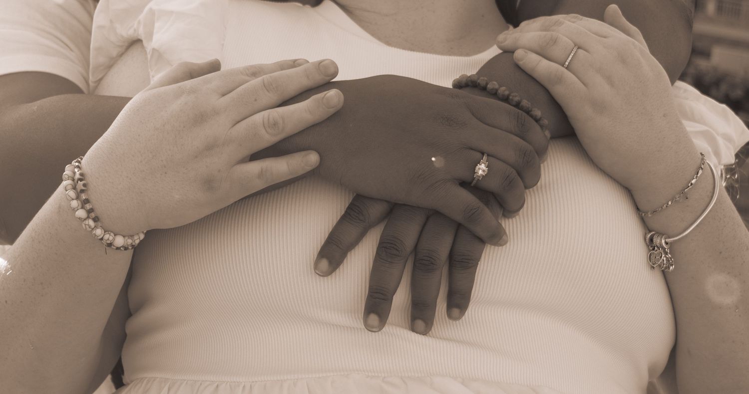 Close-up of two women's hands intertwined, wearing bracelets and a ring.