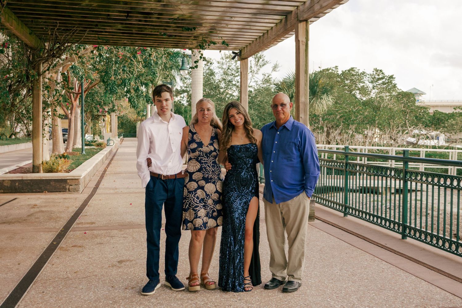 Family of four posing under a pergola walkway near a waterfront park during a formal occasion.