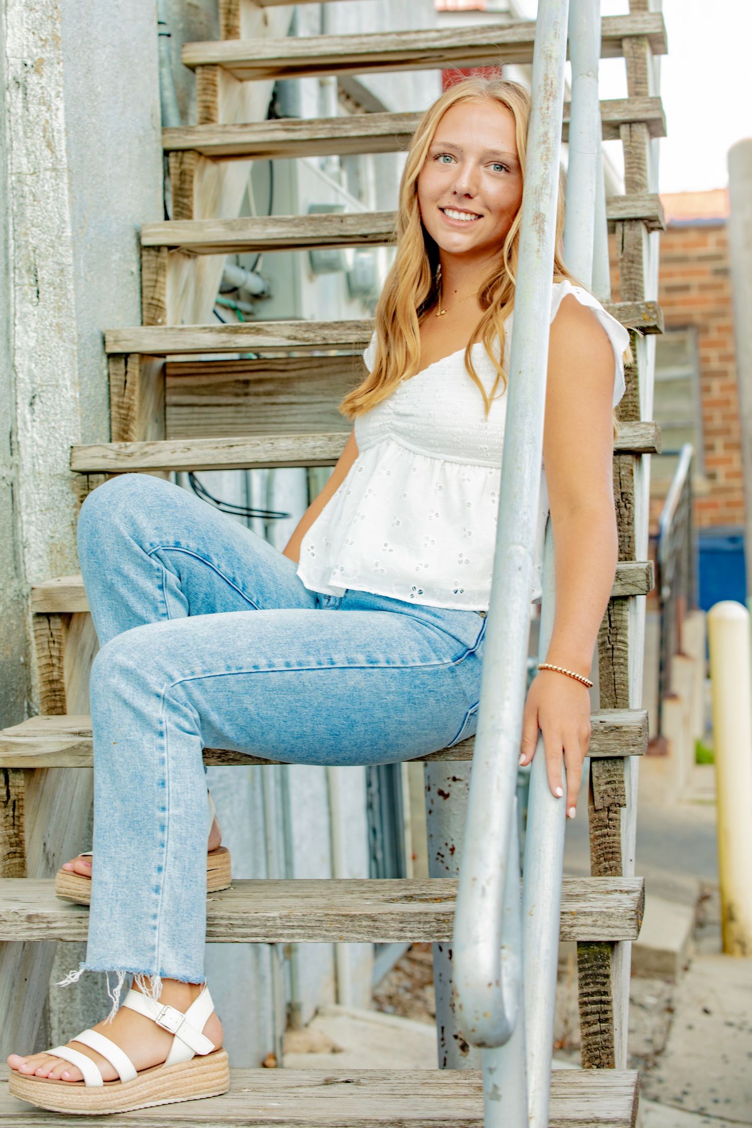 Casual summer photoshoot featuring light denim jeans and white sandals against rustic wooden stairs.