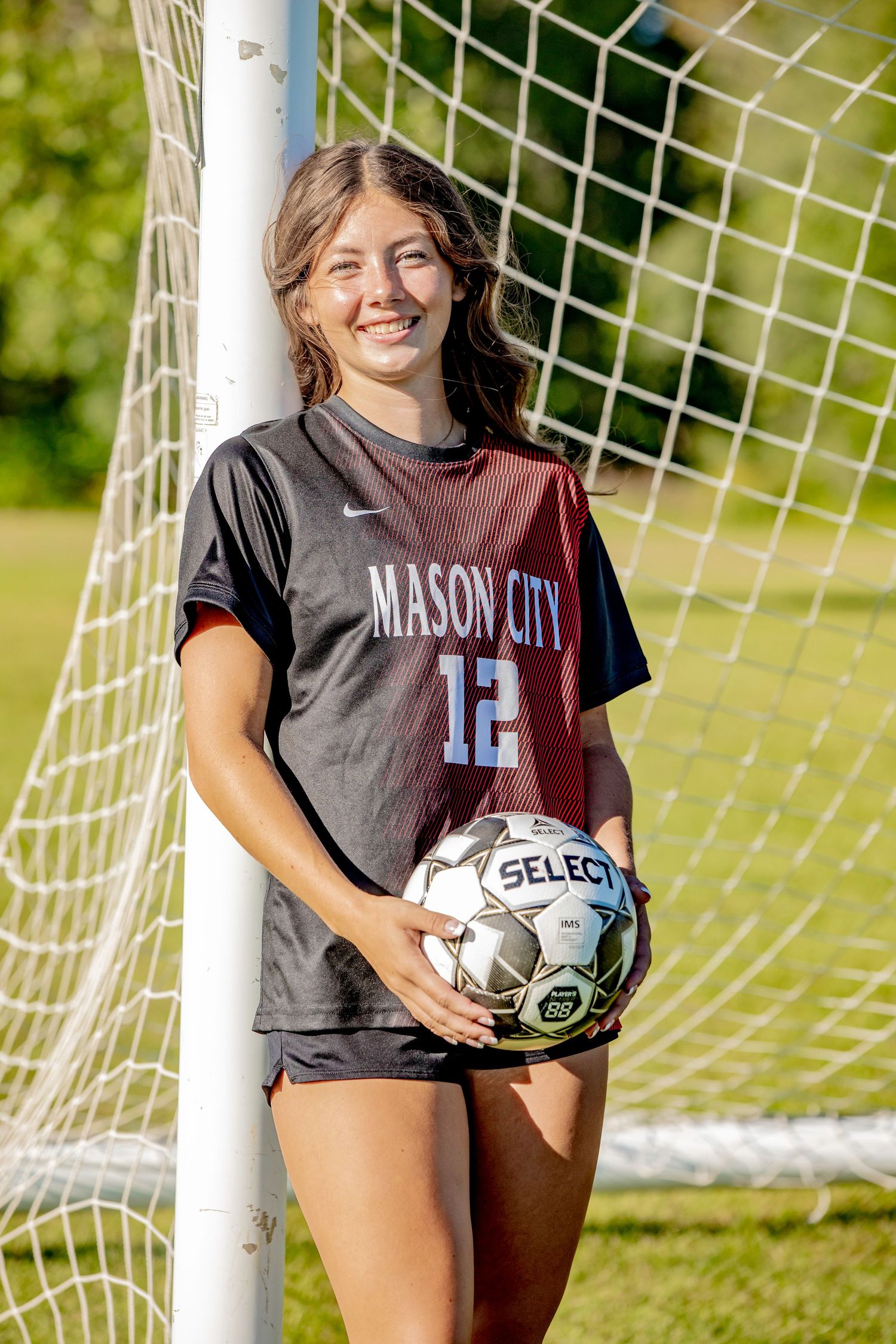 A soccer player poses with a ball in front of a goal net wearing a Mason City jersey number 12.