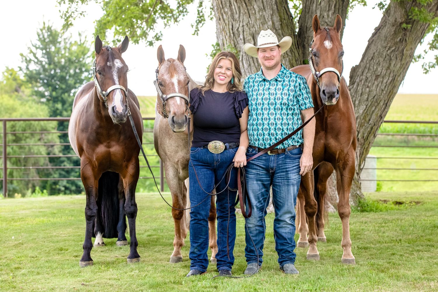 Rural portrait with four horses standing behind a couple in western attire.
