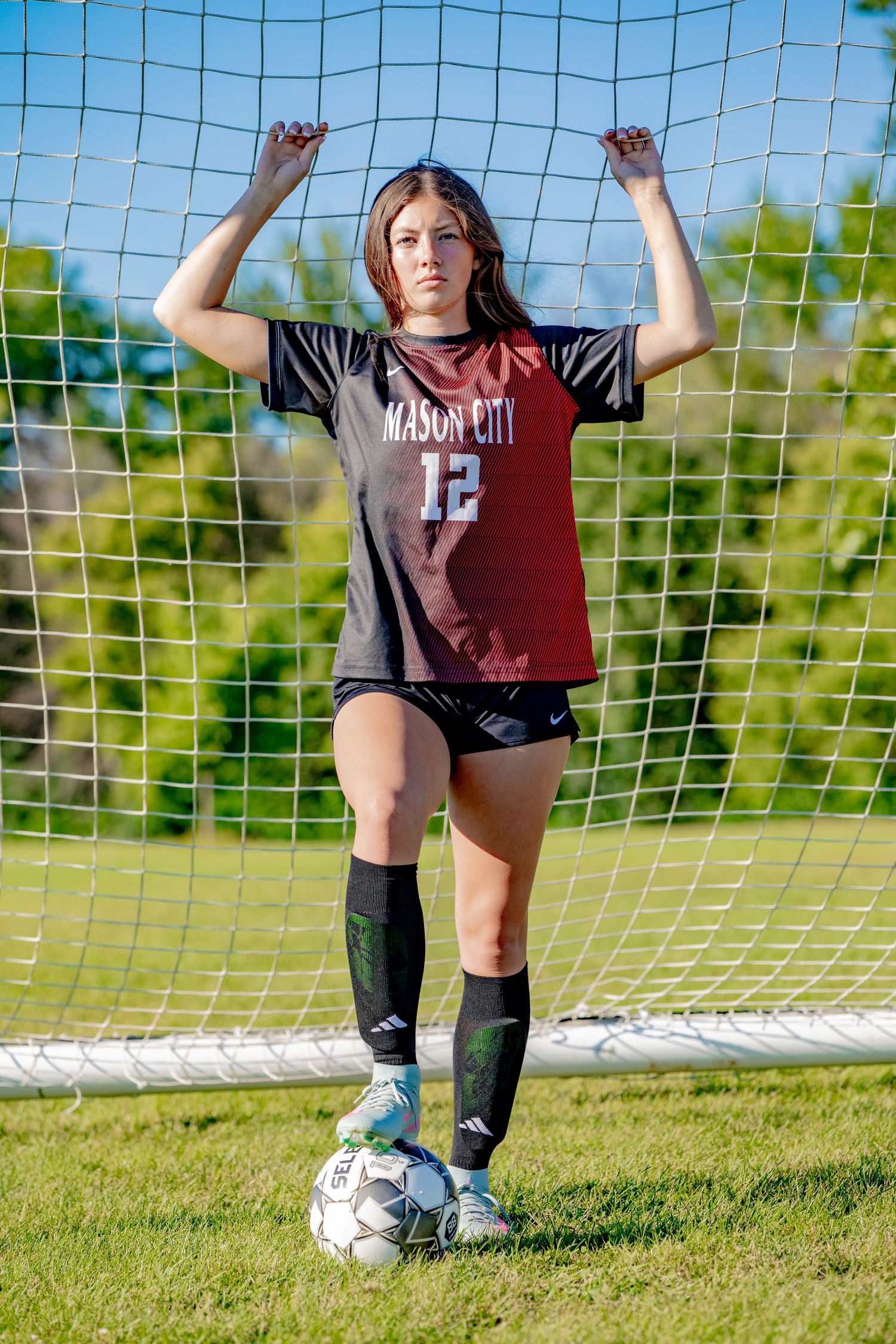 Soccer player in maroon jersey posing with soccer ball near goal net.