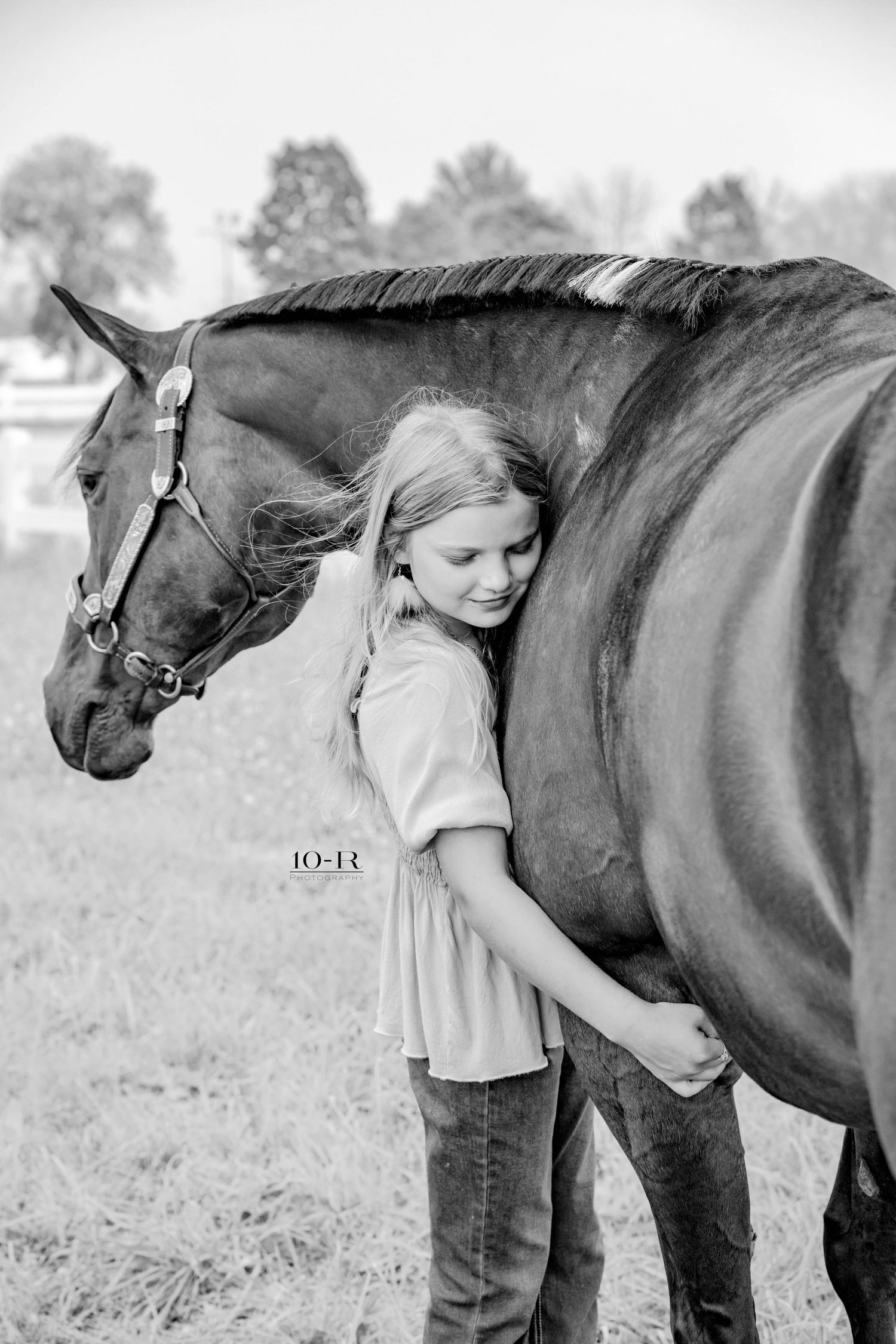 A young person in casual attire shares a tender moment with a dark brown horse in a black and white photograph.
