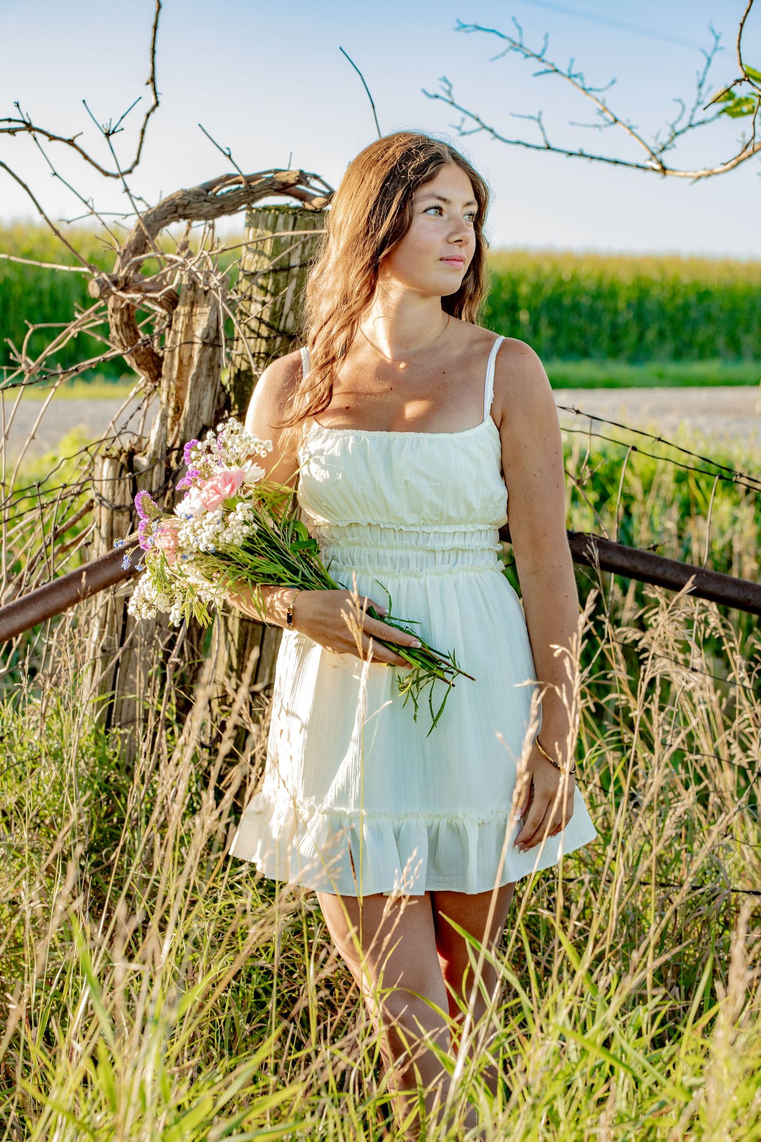A white sundress with wildflowers in a golden summer field during sunset.