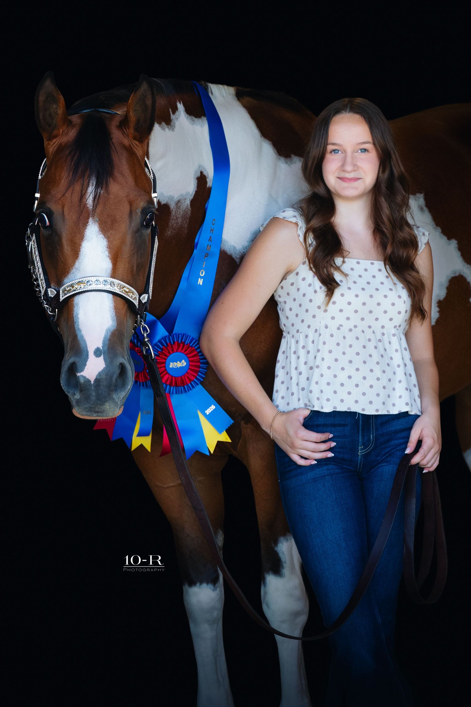 Young girl poses with award-winning paint horse displaying blue ribbon rosette against dark background.