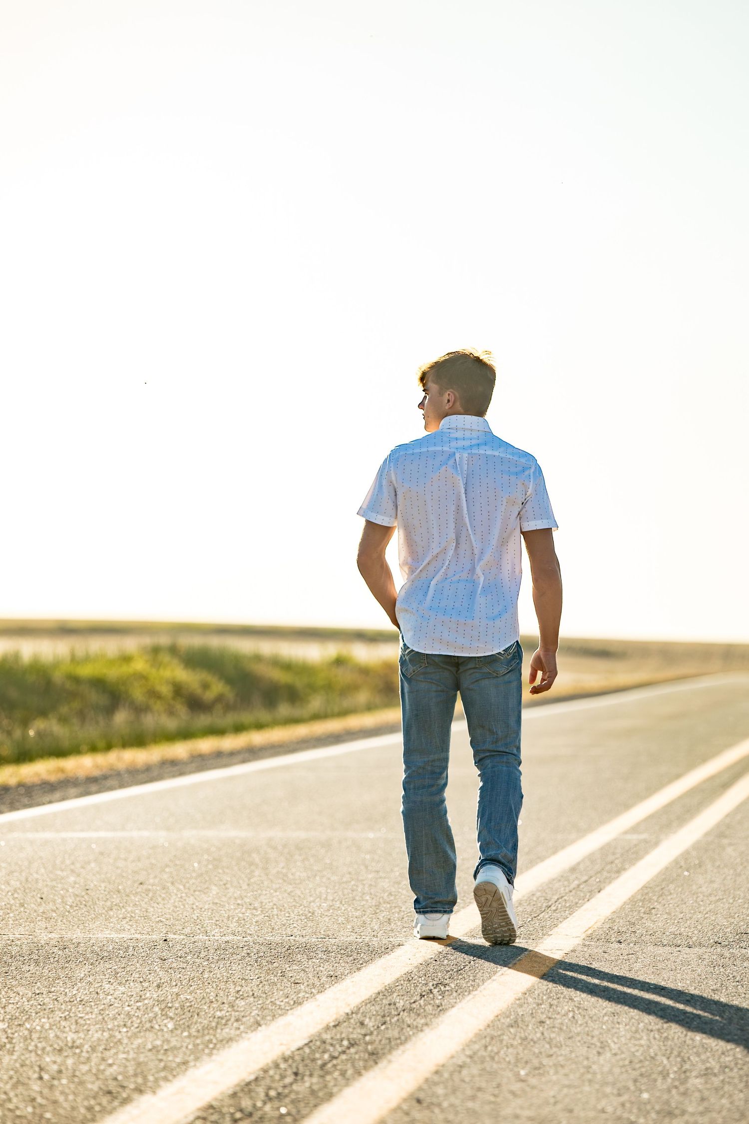 A person in a blue shirt and jeans walks along a rural road during golden hour.