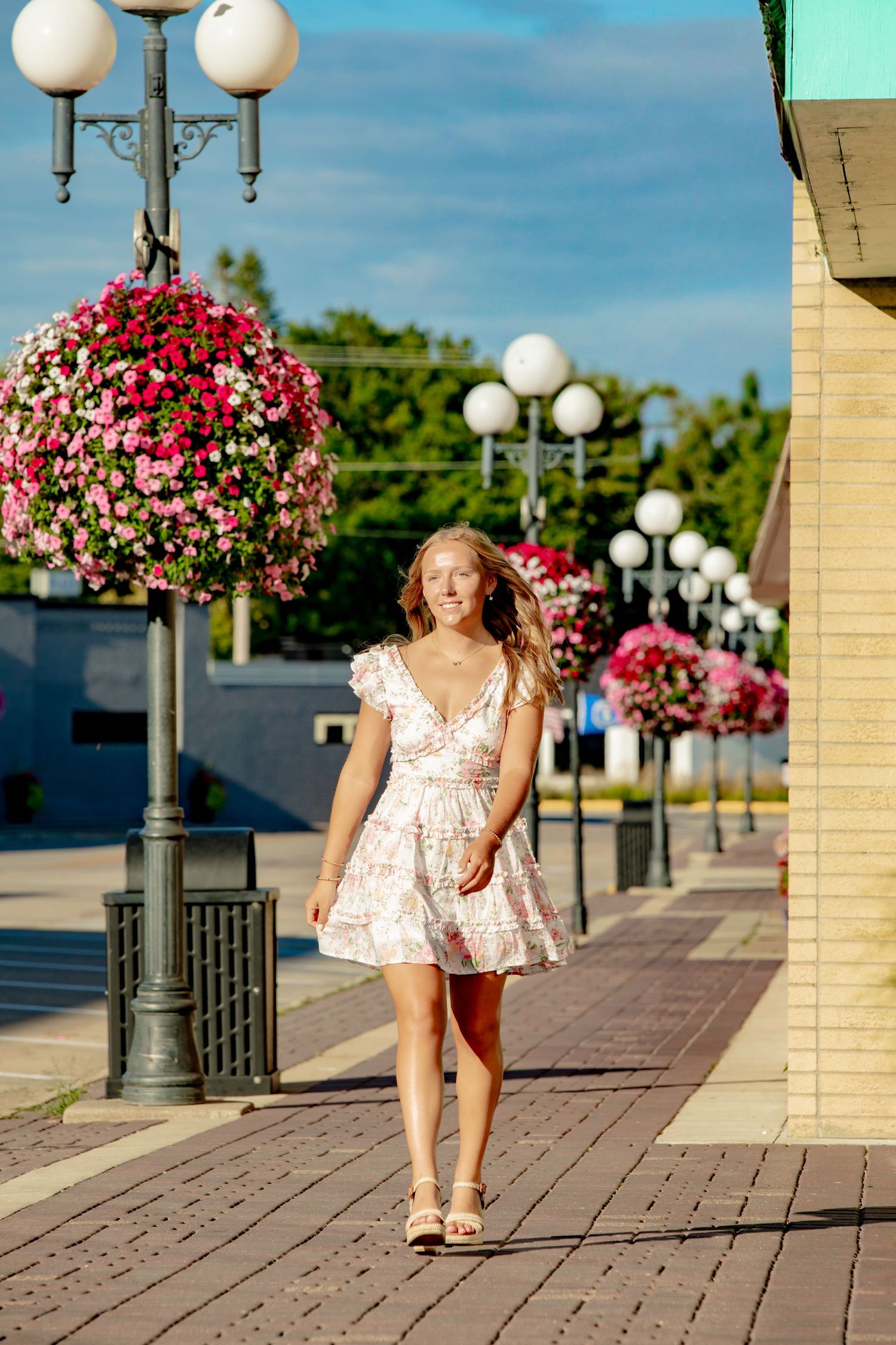 Decorative walkway with pink hanging flower baskets and white globe lamps along a brick paved path.