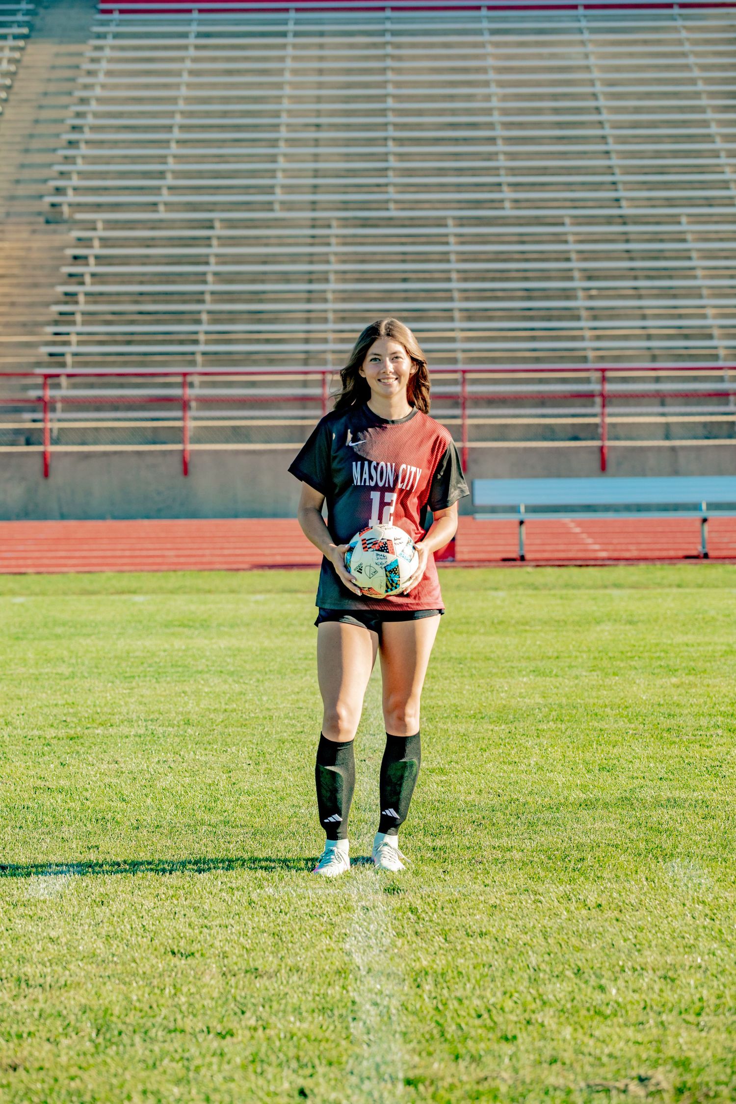 A rugby player crouches down on a grass field in a stadium with empty bleachers in the background.