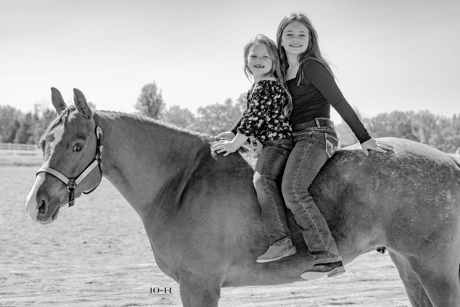 Black and white photo of two riders sharing a horseback ride together in an outdoor setting.