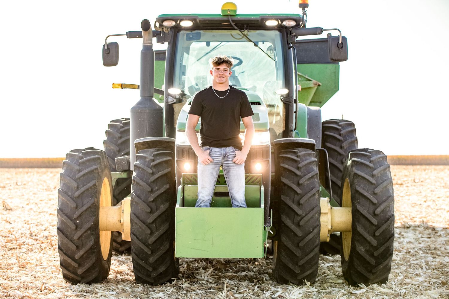 Person stands on large John Deere tractor in field during sunset.