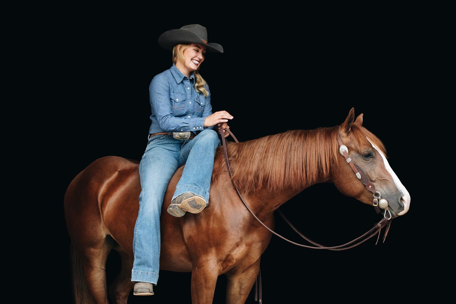 A rider in western attire sits atop a chestnut horse against a black background.