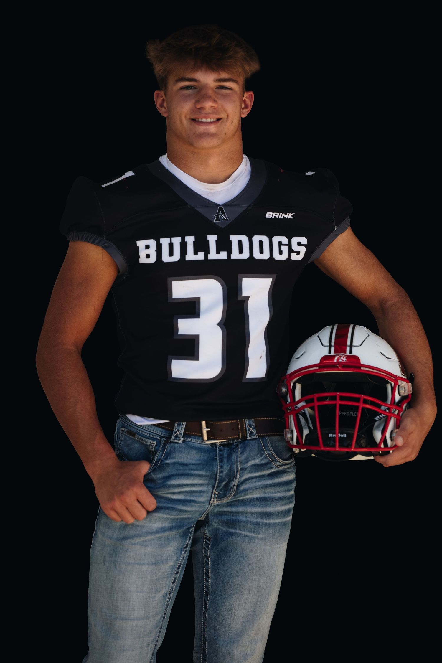 High school football player in Bulldogs jersey number 31 poses with red helmet against dark background.