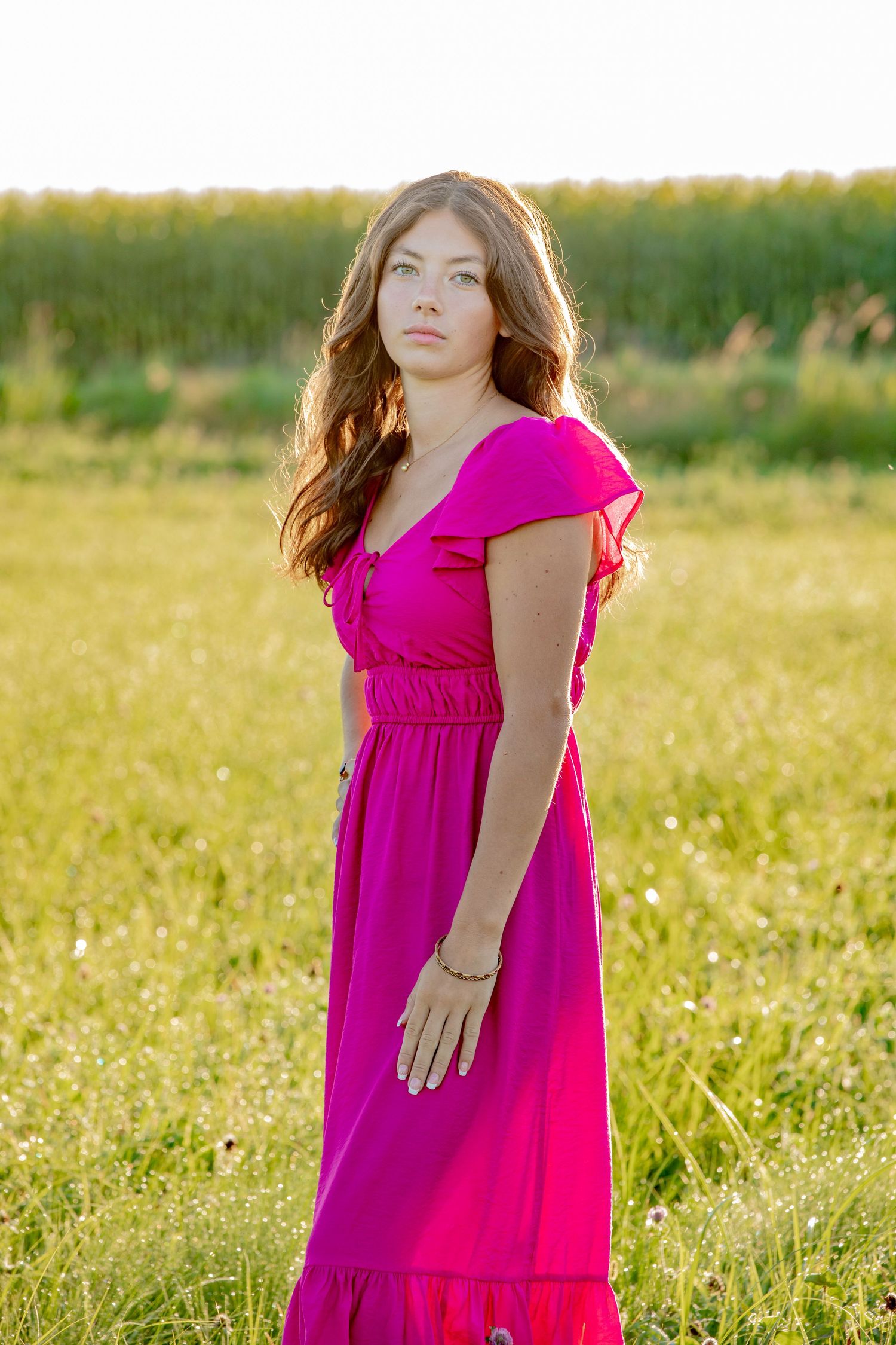 A bright fuchsia dress stands out against a golden summer field during sunset.