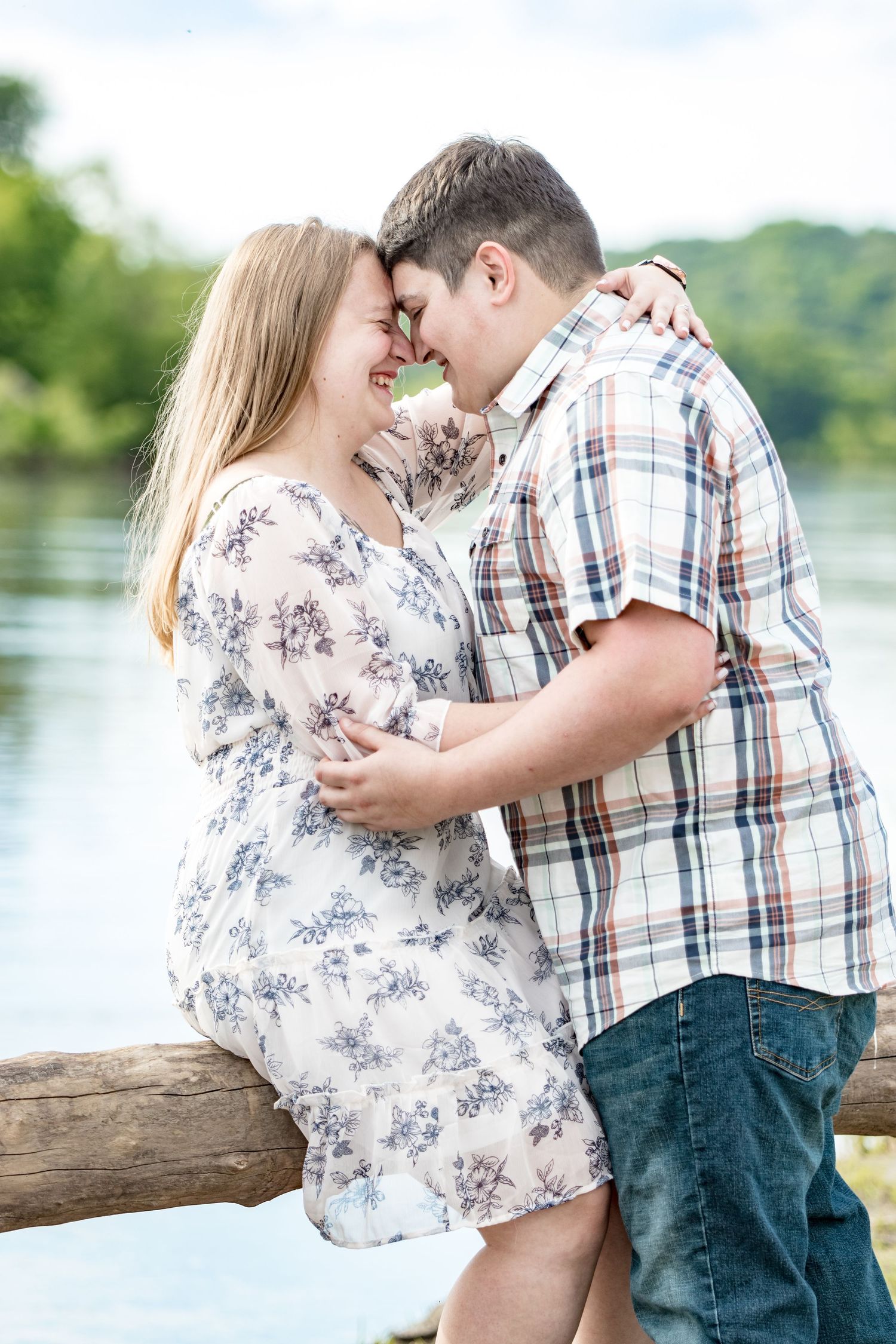 A sweet candid moment between a couple sitting on a log by the water.