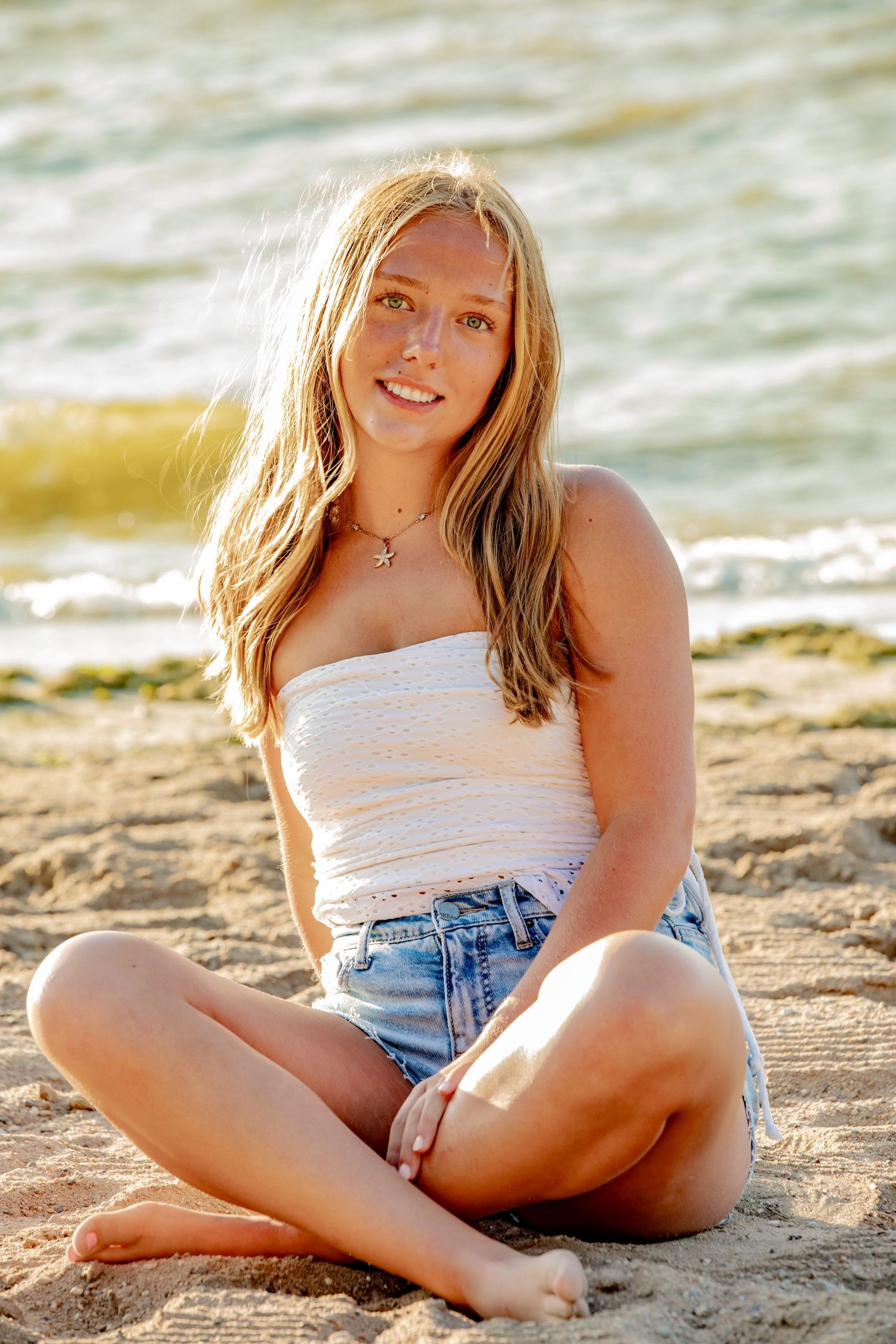 Person relaxing on sandy beach at sunset wearing casual summer attire.