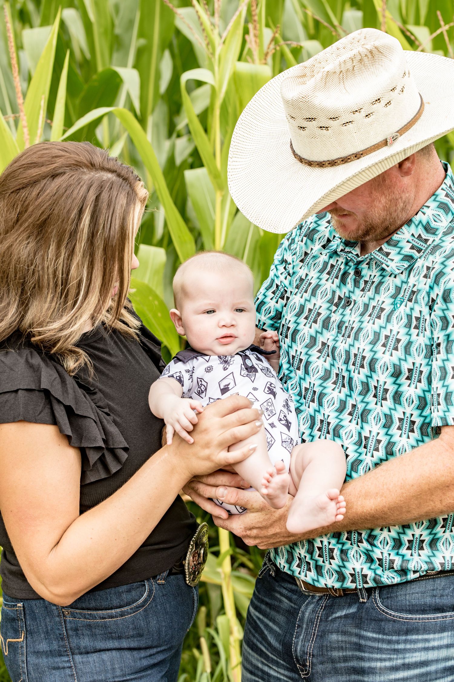 Family of three posing together in a cornfield on a bright summer day.
