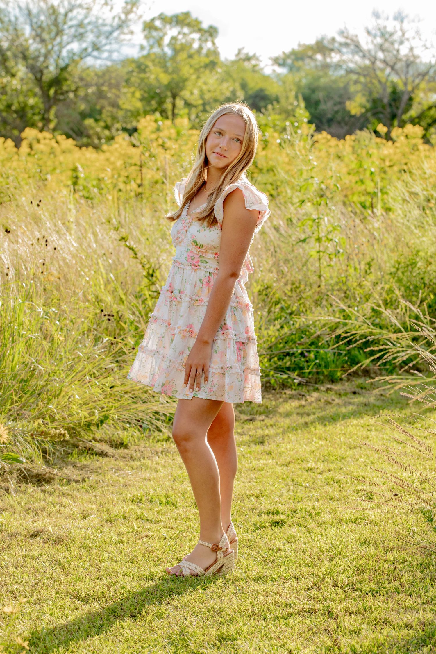 A whimsical outdoor photoshoot in a sunlit meadow wearing a floral summer dress.