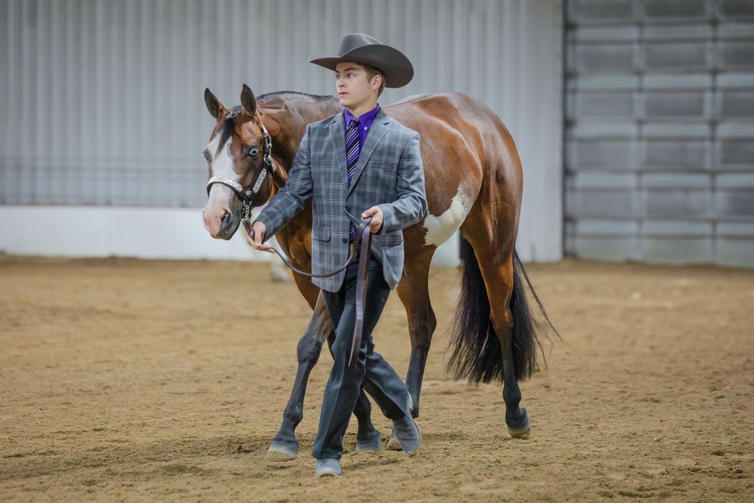 Multiple riders training their horses in an indoor riding arena with western attire.
