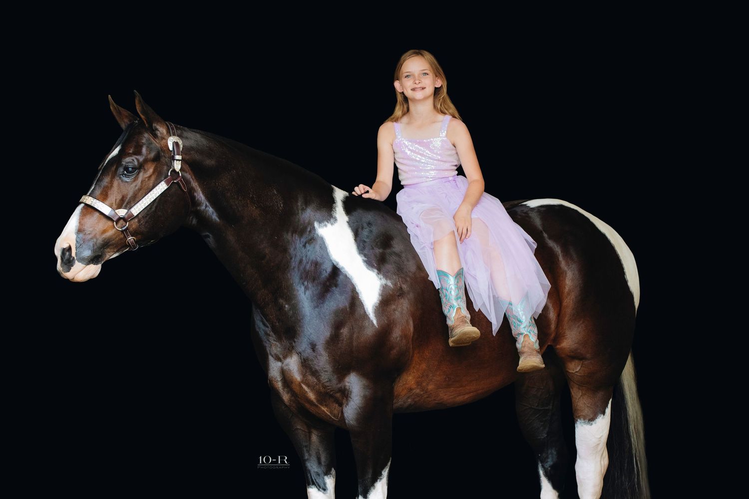 A young equestrian in a white dress rides a dark horse in a dimly lit indoor riding arena.