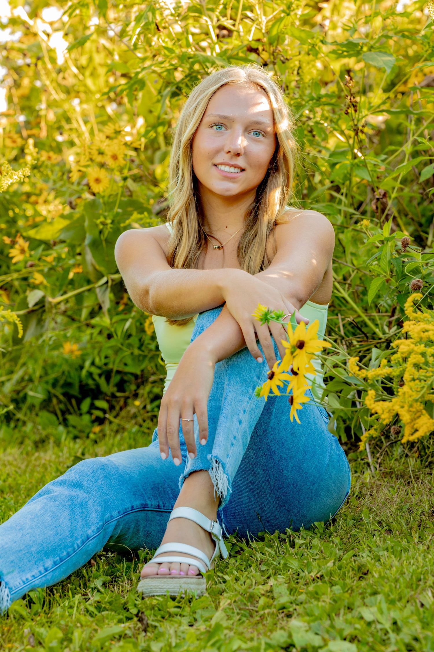 Summer portrait session in a garden with blooming yellow flowers and casual denim attire.