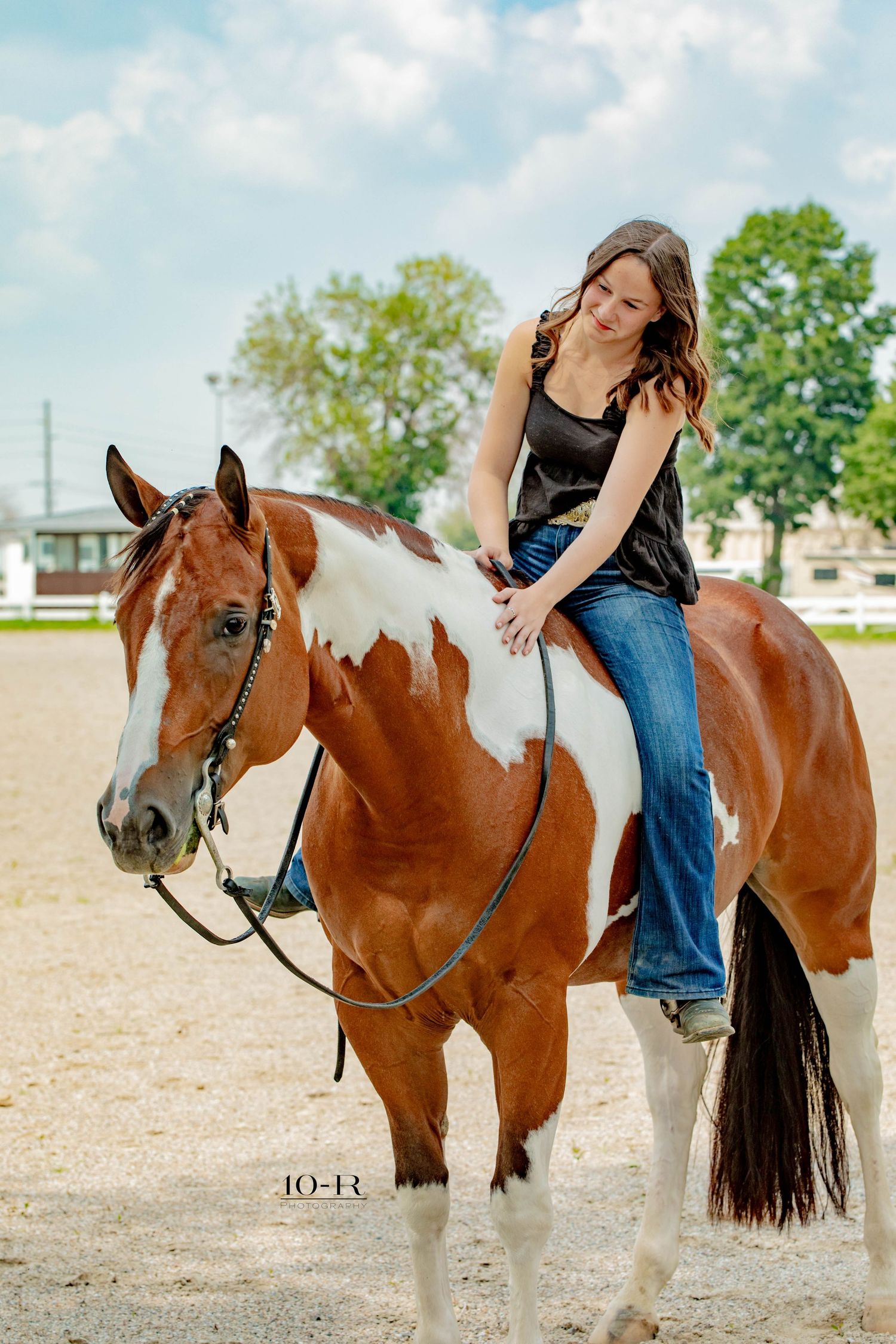 A paint horse poses with its owner in a rustic outdoor setting during a photo session.
