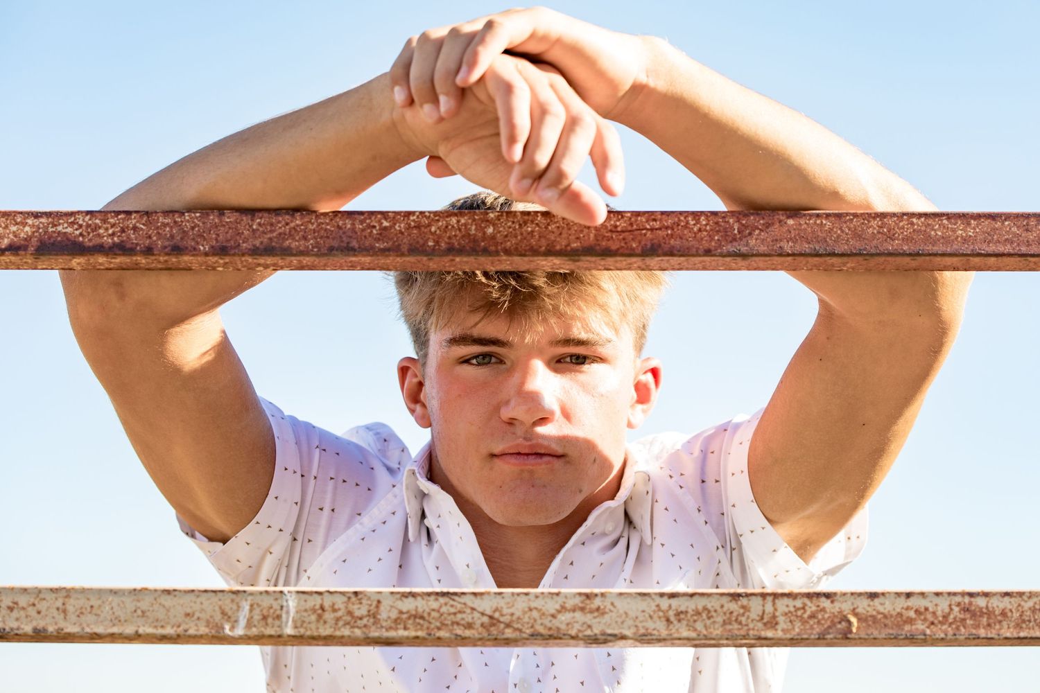 Person leaning on wooden fence rail against bright sunny background.
