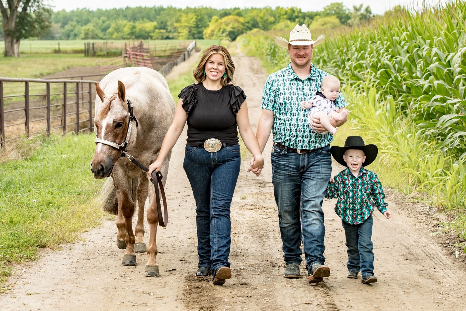 Family walking down country path with cream colored horse on sunny day.