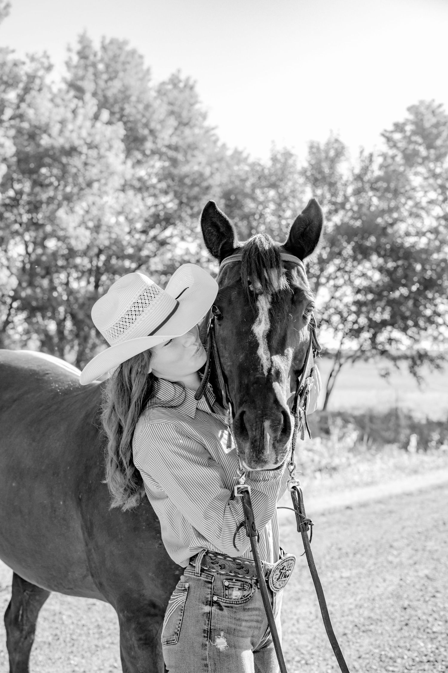 Black and white photo of a horse and rider in western attire against a wooded background.