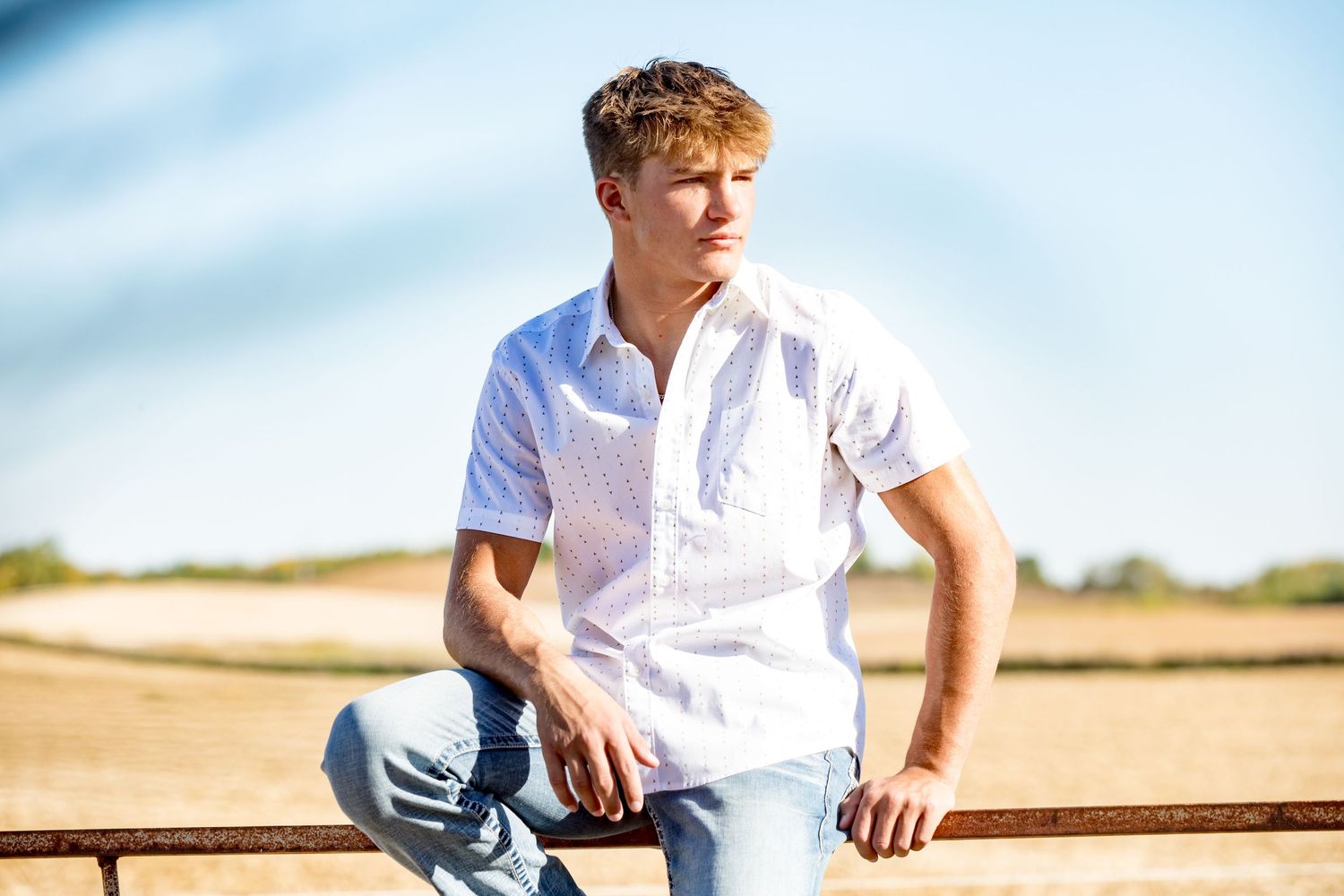 Person in white short-sleeve shirt sits casually outdoors on sunny day.