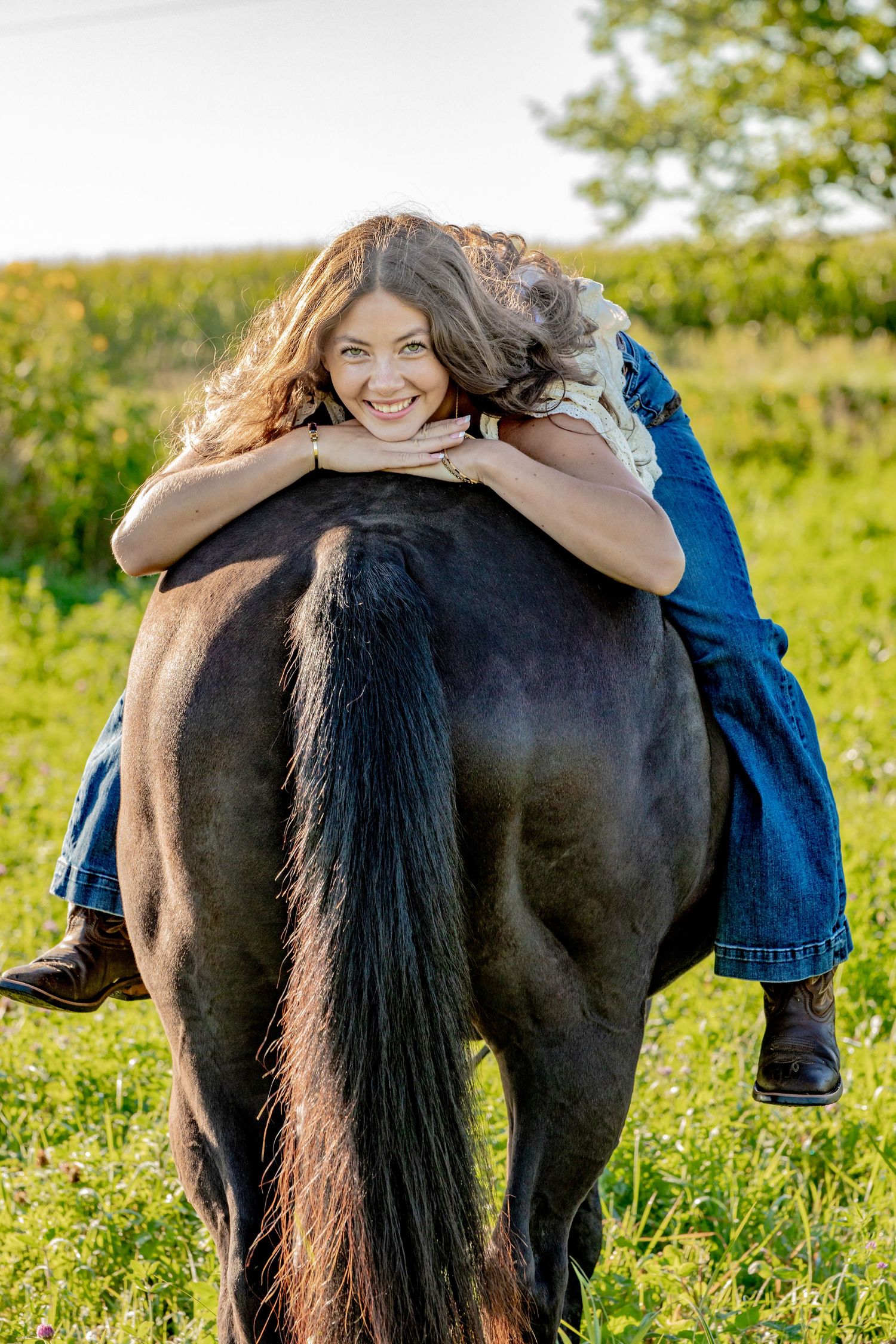Someone sitting cross-legged on the back of a dark horse in a sunny field.