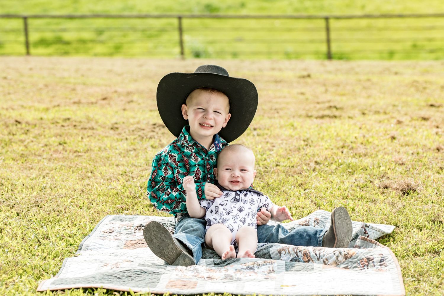 Two young children in western wear sitting together on blanket outdoors.