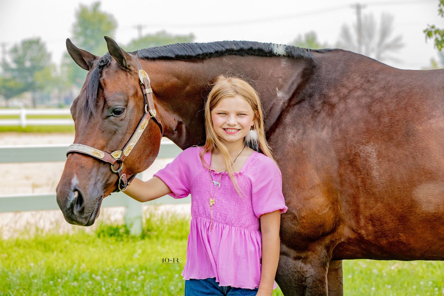 A young equestrian in pink stands with a bay horse in a sunny pasture, sharing a tender moment together.