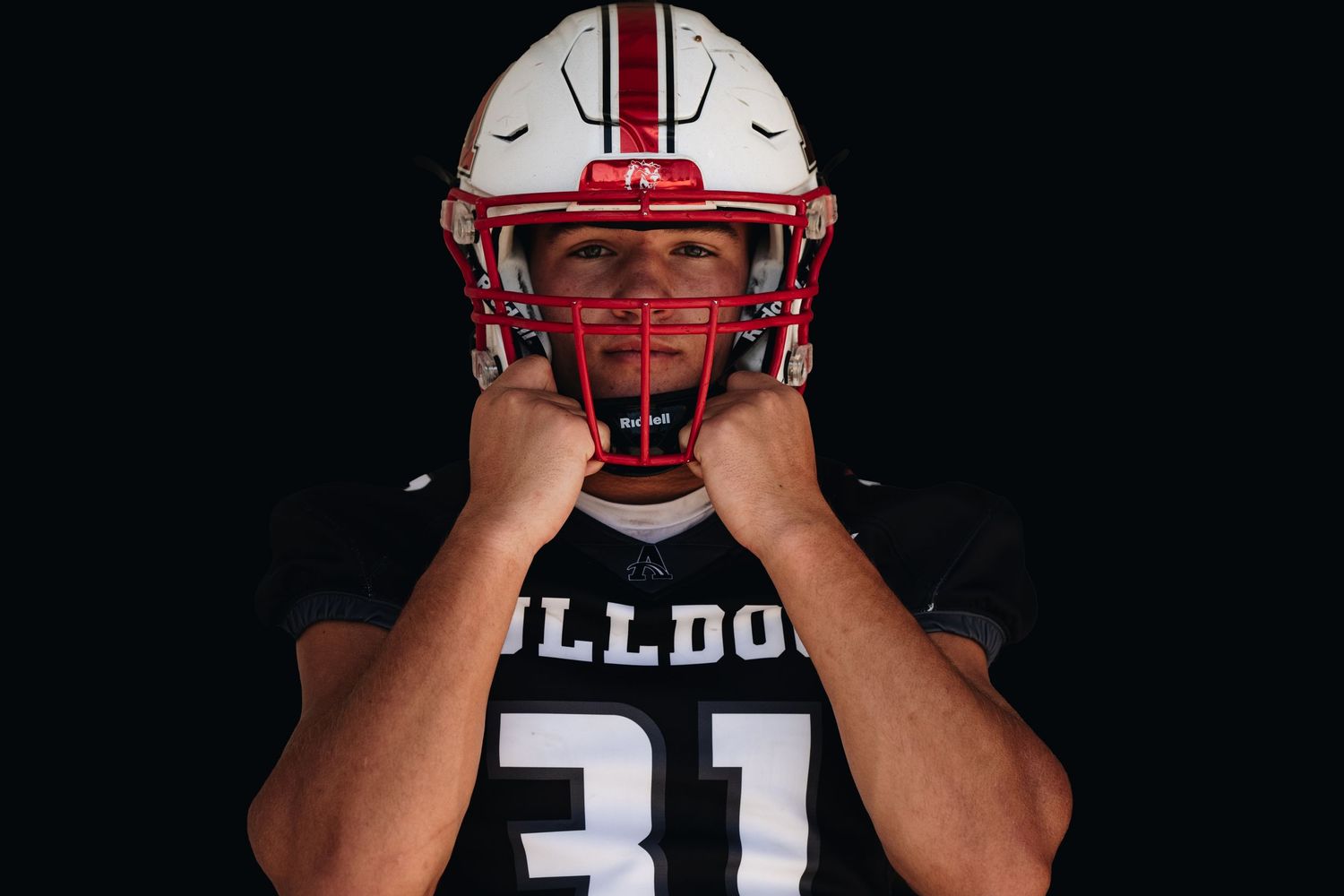 Football player in black Bulldogs uniform holds face mask of red and white helmet.