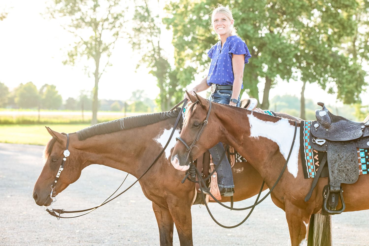 A horse and rider against golden sunlit trees on a dirt path at sunset.