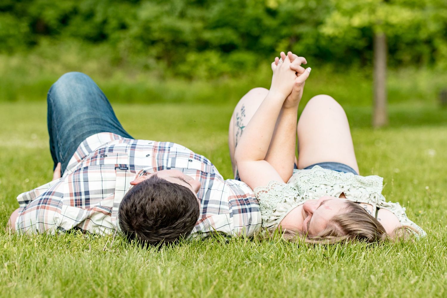A couple lies in the grass on a summer day, sharing a relaxed moment together.