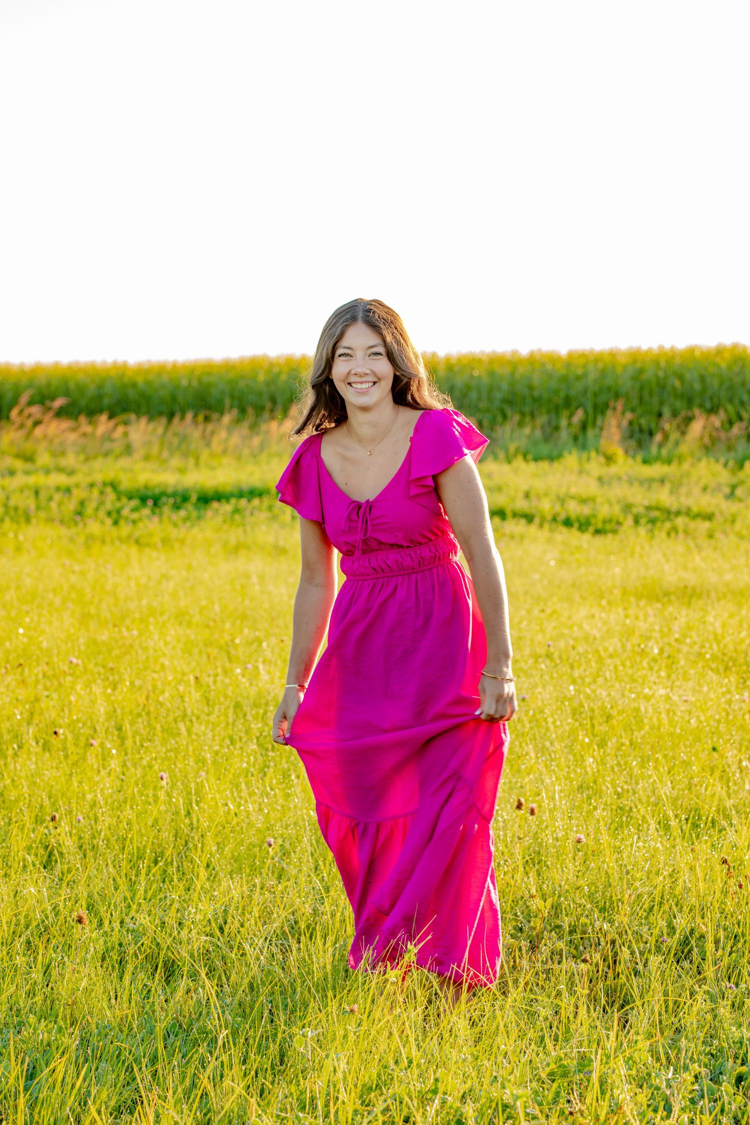 A person in a bright pink flowing dress runs joyfully through a sunlit meadow of tall golden grass.