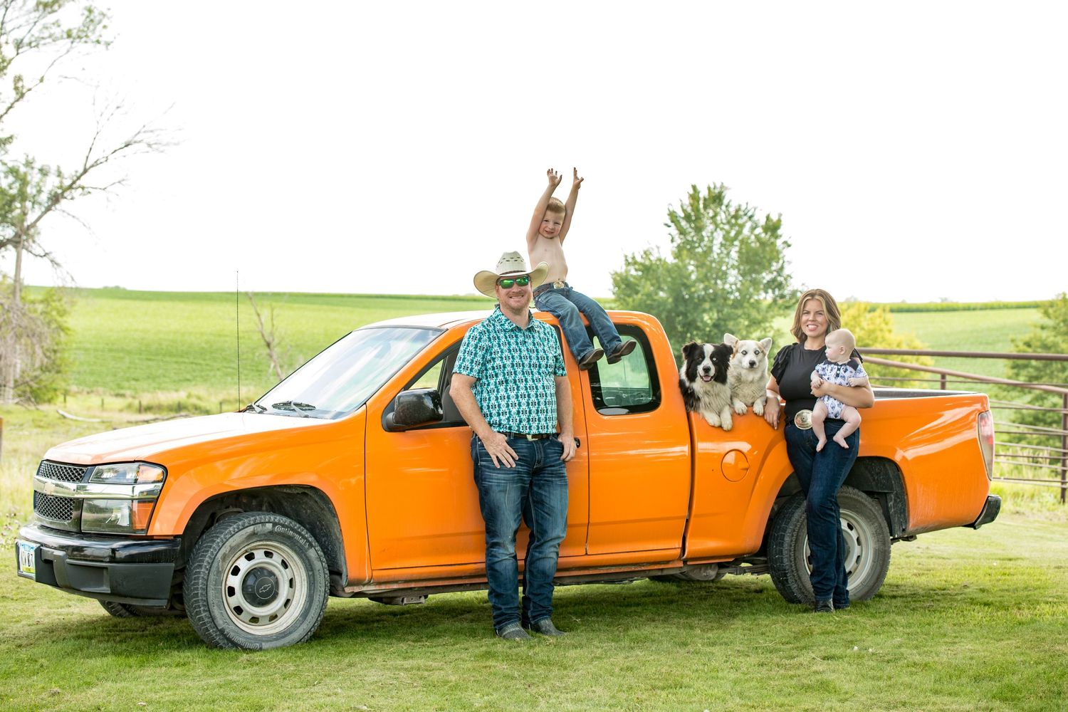 Family posing next to an orange pickup truck in a rural setting.