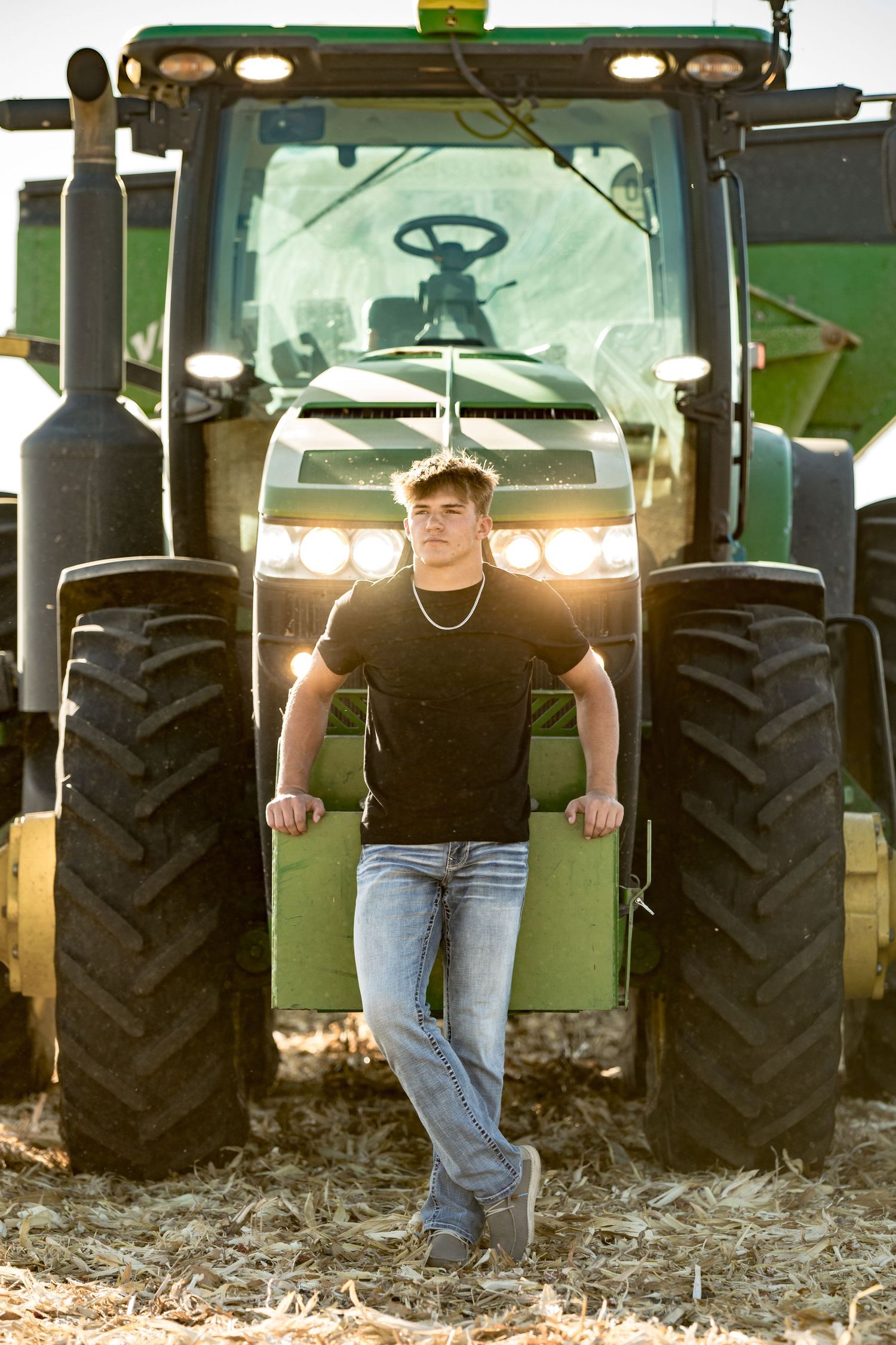 Athletic figure poses in front of large green tractor with sunset backlighting.